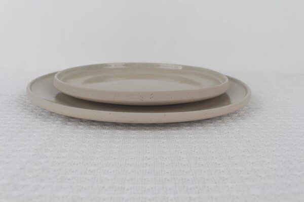 Two stacked Sandstone beige speckled stoneware dinner plates with raised rims and minimalist design