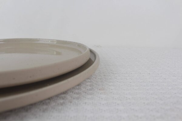 Close-up of stacked Sandstone stoneware plates showing beige speckled glaze and smooth raised edges