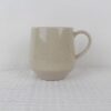 Sandstone beige speckled stoneware coffee mug with curved handle, tapered base and glossy finish