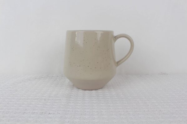 Sandstone beige speckled stoneware coffee mug with curved handle, tapered base and glossy finish